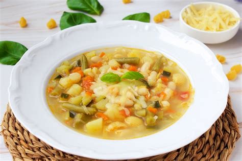 Sopa minestrone humeante en un cuenco con ingredientes frescos alrededor