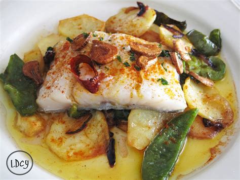 Plato de bacalao al horno decorado con berenjenas y cebolla sobre una mesa de madera
