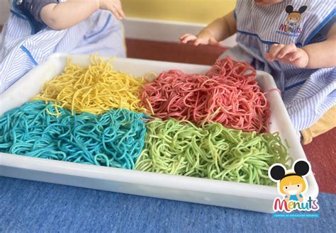 Bebé jugando con espaguetis de colores en una bandeja