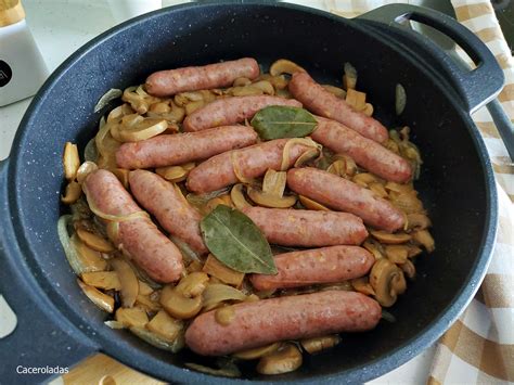 Salchichas doradas en una sartén con cebolla y champiñones
