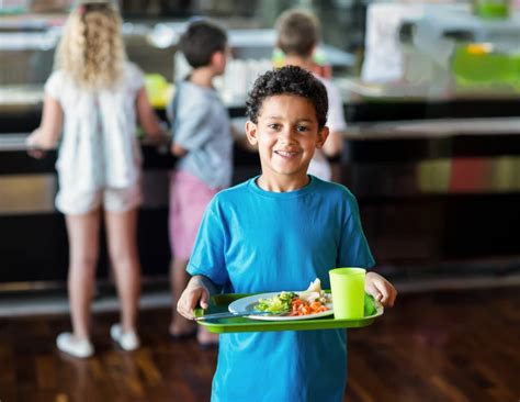 Niño en el comedor escolar con un plato de comida sin terminar