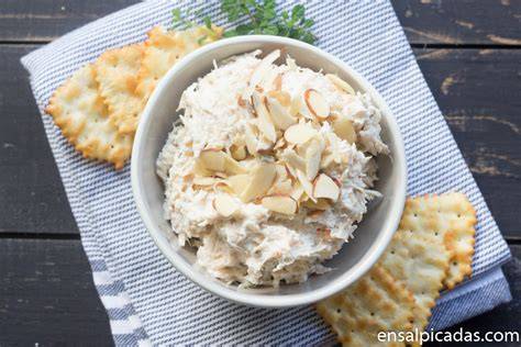 Plato de dip de pollo con queso crema y cilantro rodeado de galletas saladas y vegetales