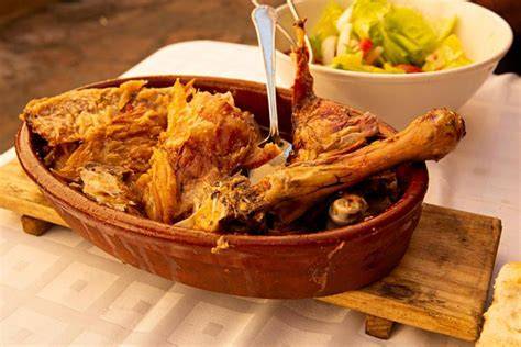 Detalle de cordero asado servido en fuente de barro