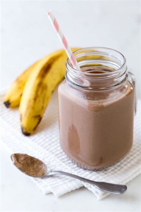 Batido proteico de chocolate y plátano en un vaso, con plátanos y cacao en polvo alrededor.