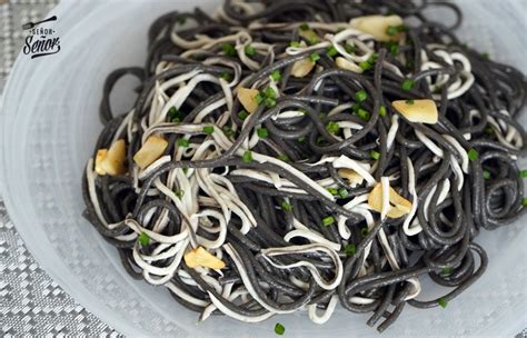 Mesa con espaguetis negros con marisco y una copa de vino blanco