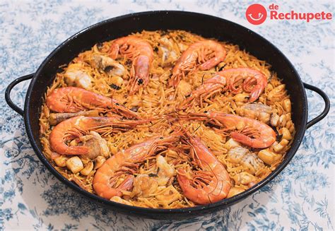Mesa con paellera de fideuá de sepia y gambas con alioli casero y rodajas de limón.