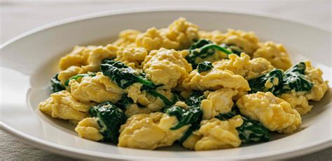 Huevos rompiéndose en una sartén con espinacas