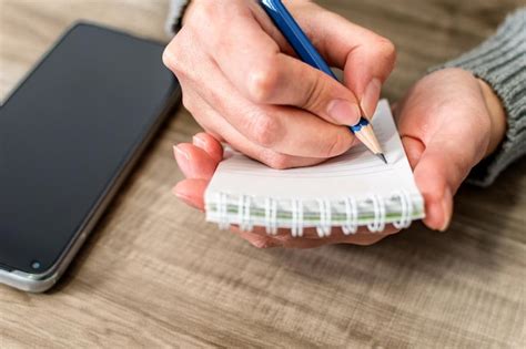 Mano escribiendo notas en un cuaderno junto a un teléfono