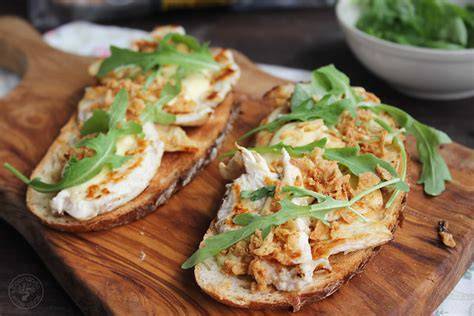 Tosta de pollo terminada con cebolla crujiente y rúcula