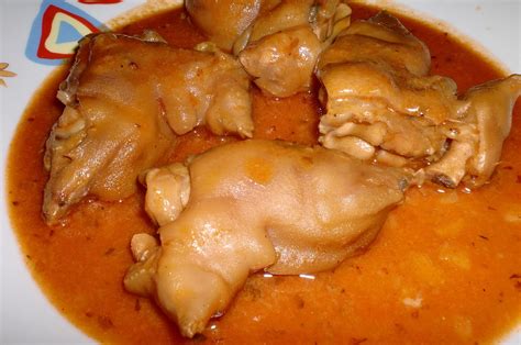Plato de manitas de cerdo en salsa de tomate servido en cazuela de barro