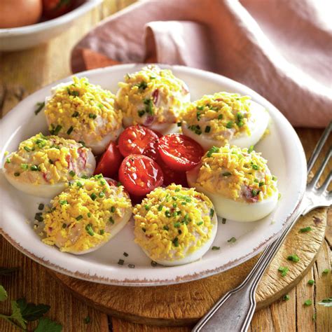 Plato de huevos rellenos de atún decorados con tomate frito y hierbas frescas