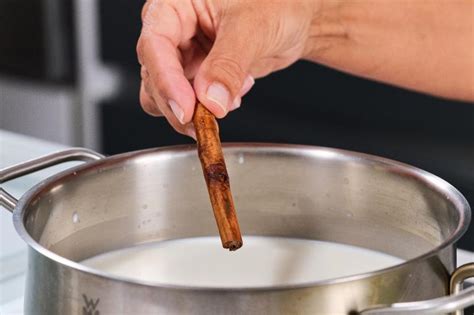 Leche calentándose en un cazo con rama de canela y piel de limón para infusionar