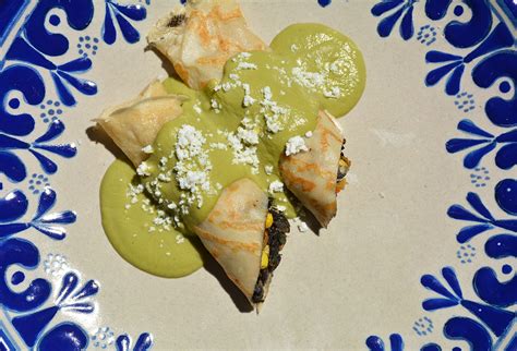 Plato elegante de crepas rellenas de flor de calabaza y huitlacoche con salsa poblana