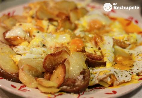 huevos rotos servidos con queso rallado y tomate
