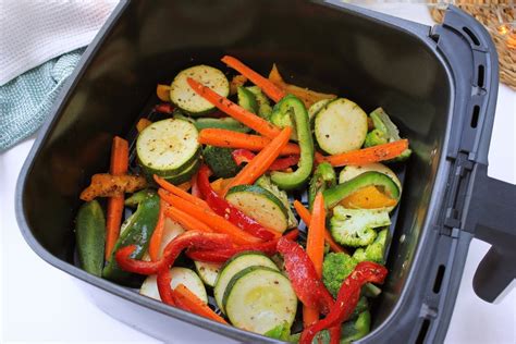 Proceso de colocación de pollo y verduras en la cesta de la freidora de aire
