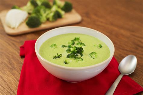 Crema de brócoli en un tazón blanco con ingredientes frescos alrededor