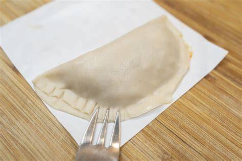 Persona sellando los bordes de una empanadilla con un tenedor