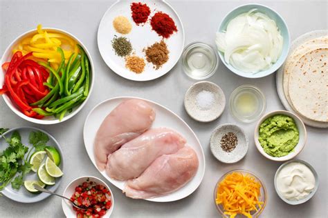 Mesa con diferentes ingredientes para fajitas, incluyendo pollo, pimientos, cebolla, tortillas y salsas