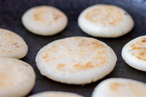 Masa de arepa y arepas cocinándose en la sartén