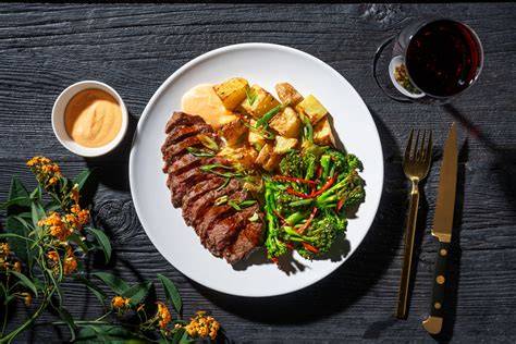 Plato de carne roja servido junto a una botella de cerveza La Goudale
