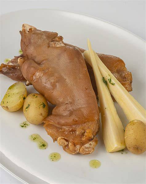 Plato de manitas de cerdo en salsa servido con guarnición