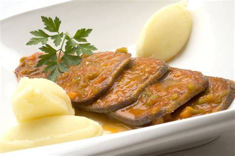 Plato de lengua en salsa de tomate servido con guarnición