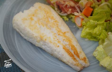 Detalle de la merluza horneada con la capa de mayonesa dorada y salsa de pimientos al fondo