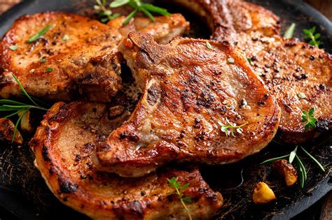 Chuletas de cerdo fritas doradas sobre una tabla de cortar con hierbas aromáticas