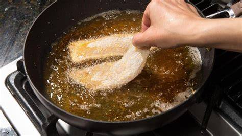 Persona friendo pescado en una sartén