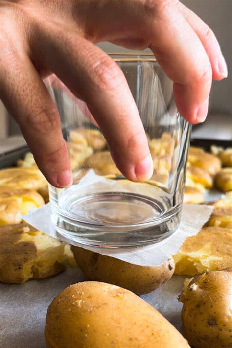 Proceso de aplastado de patatas cocidas con un vaso sobre bandeja de horno