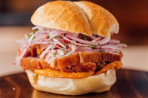 Plato de pan con chicharrón peruano servido con salsa criolla y camote frito