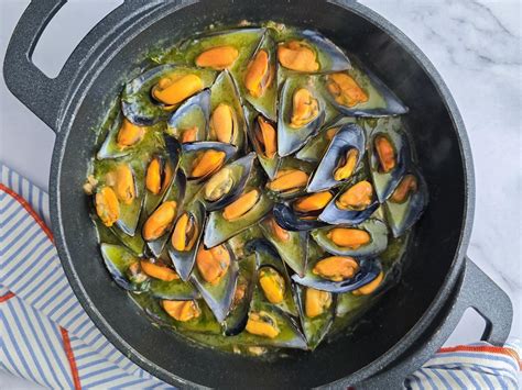 Plato de mejillones en salsa verde servido con pan y vino blanco