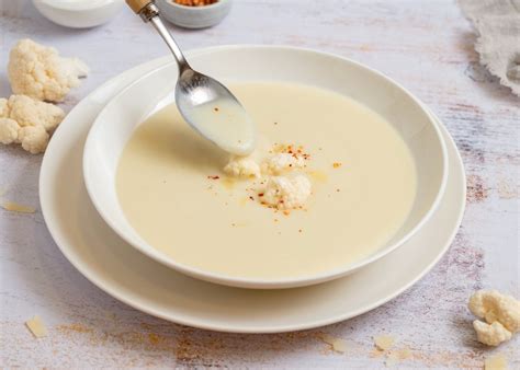 Crema de coliflor decorada con láminas de ajo negro sobre un plato de diseño