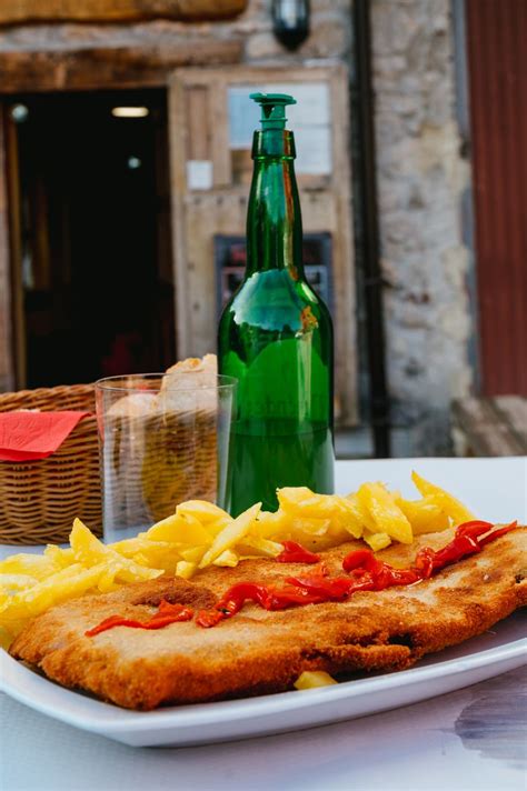 Mesa con cachopo, patatas fritas y botella de sidra