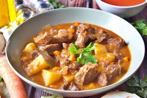 Plato de carne guisada con zanahorias y aceitunas servido en una cazuela de barro
