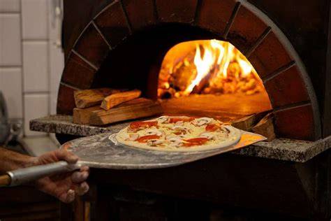 Chef preparando pizza artesanal en un horno de leña