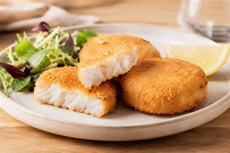 Plato de medallones de merluza rebozados dorados y crujientes servidos con ensalada