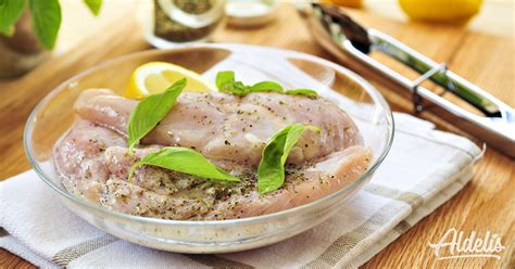 Pollo entero marinado en un bol con naranjas y hierbas aromáticas