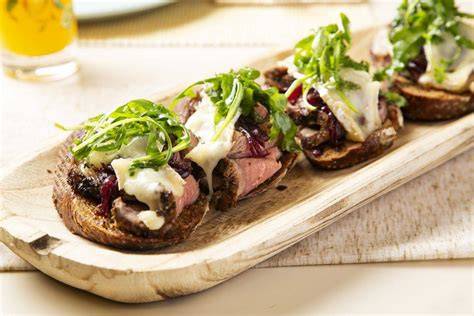Composición de sándwich con roast beef, cebolla caramelizada y tomate sobre pan thins