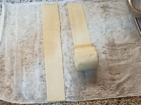 Tiras de hojaldre crudas sobre papel de horno, pintadas con glasa y almendra